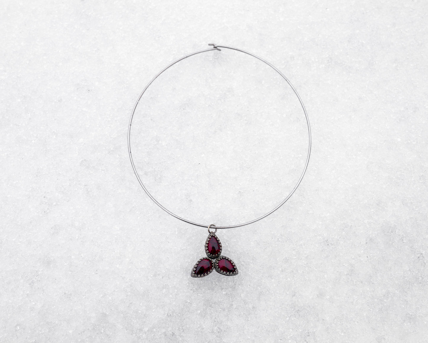 Choker-style wire necklace featuring a trinity formation of three pear-cut bloody bison jasper stones in dark silver bezels. The symmetrical pendant is styled flat on a snowy surface, radiating sacred geometry and ancestral energy.