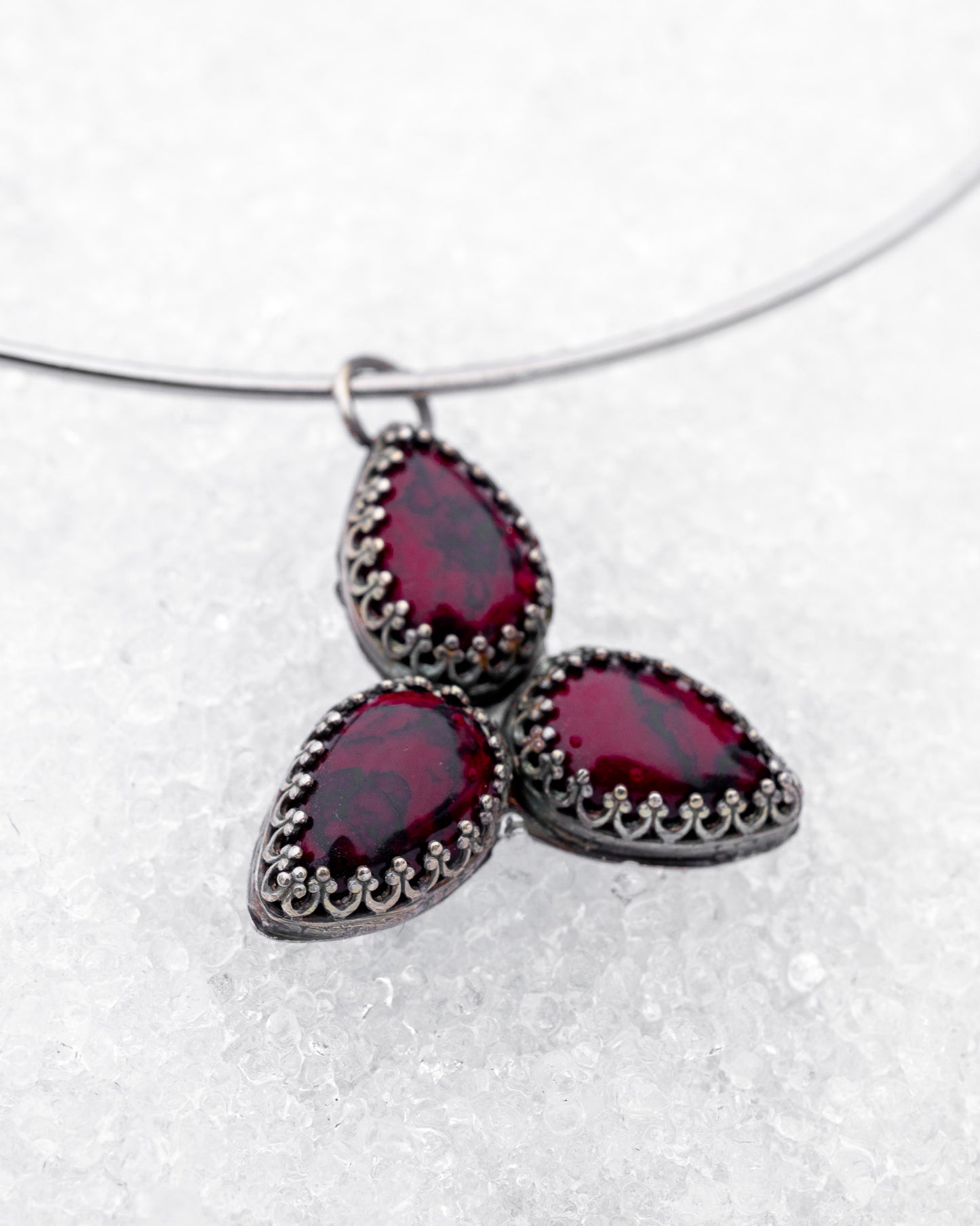 Choker-style wire necklace featuring a trinity formation of three pear-cut bloody bison jasper stones in dark silver bezels. The symmetrical pendant is styled flat on a snowy surface, radiating sacred geometry and ancestral energy.