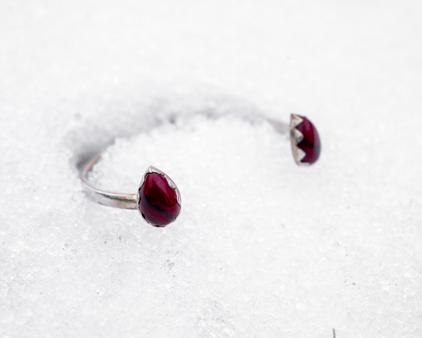 Open sterling silver cuff bracelet with two teardrop-shaped bloody bison jasper stones in jagged fang-like bezels. Photographed resting in white snow, the cuff evokes a fierce, protective energy and vampiric elegance.