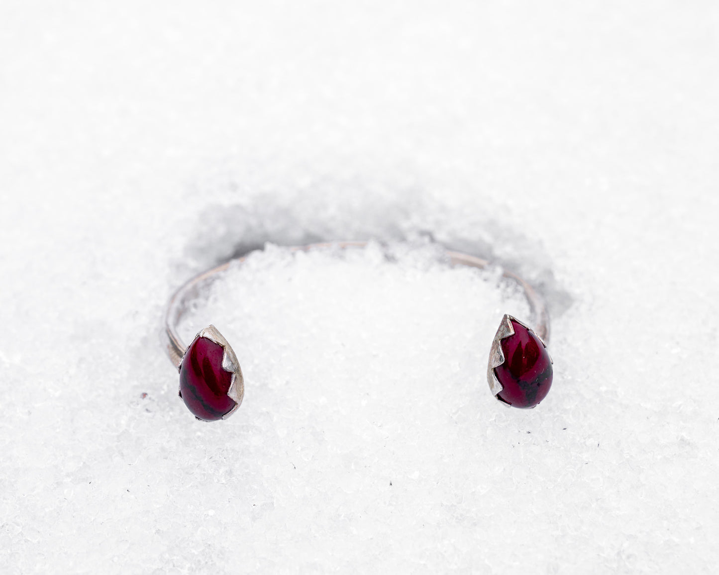 Open sterling silver cuff bracelet with two teardrop-shaped bloody bison jasper stones in jagged fang-like bezels. Photographed resting in white snow, the cuff evokes a fierce, protective energy and vampiric elegance.