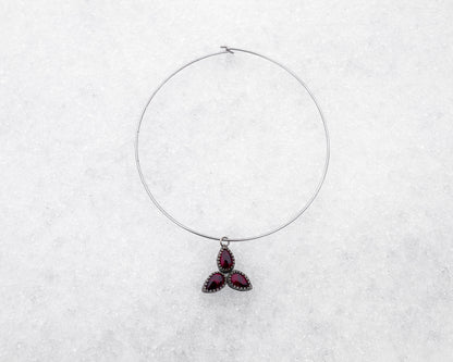 Choker-style wire necklace featuring a trinity formation of three pear-cut bloody bison jasper stones in dark silver bezels. The symmetrical pendant is styled flat on a snowy surface, radiating sacred geometry and ancestral energy.
