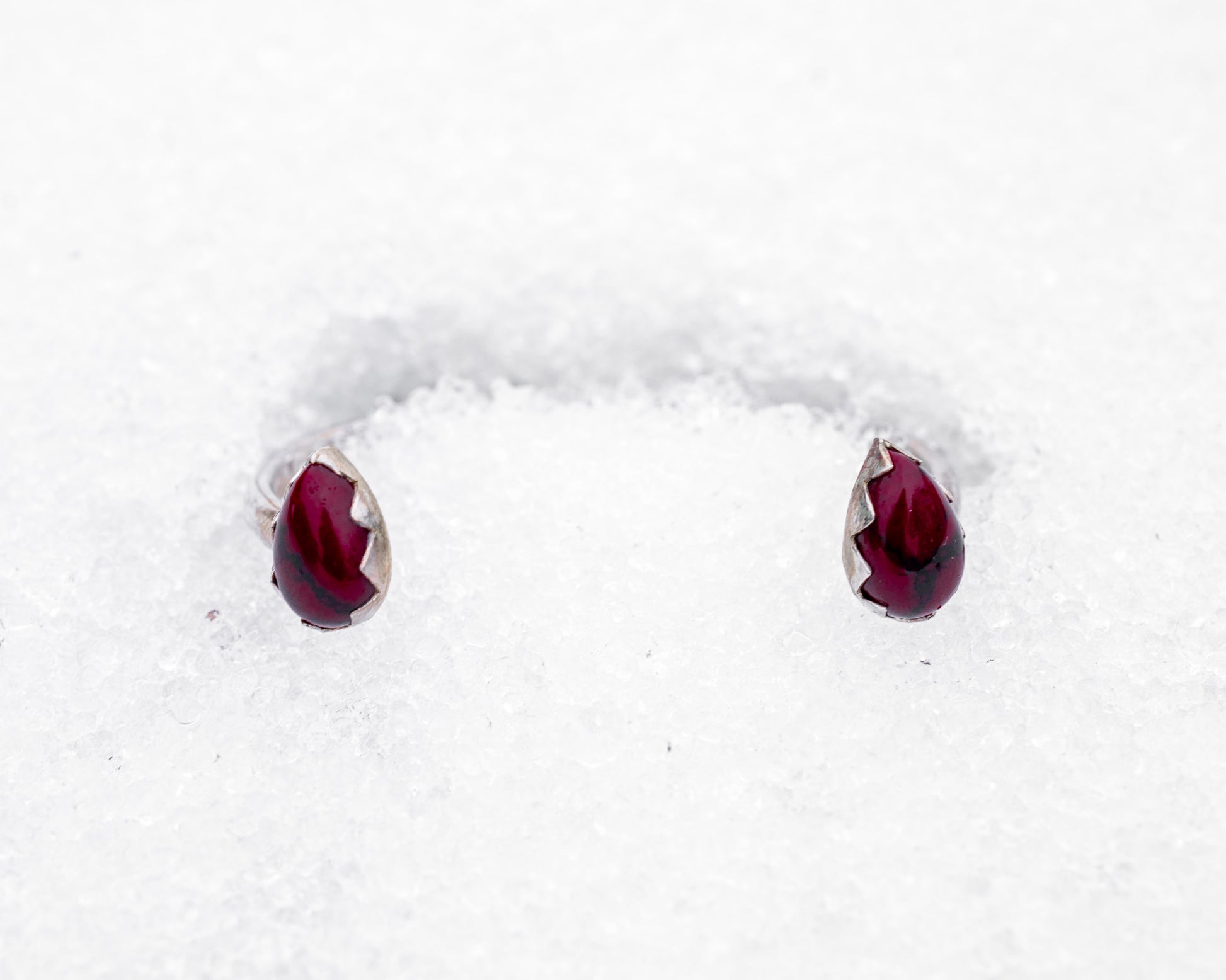 Open sterling silver cuff bracelet with two teardrop-shaped bloody bison jasper stones in jagged fang-like bezels. Photographed resting in white snow, the cuff evokes a fierce, protective energy and vampiric elegance.
