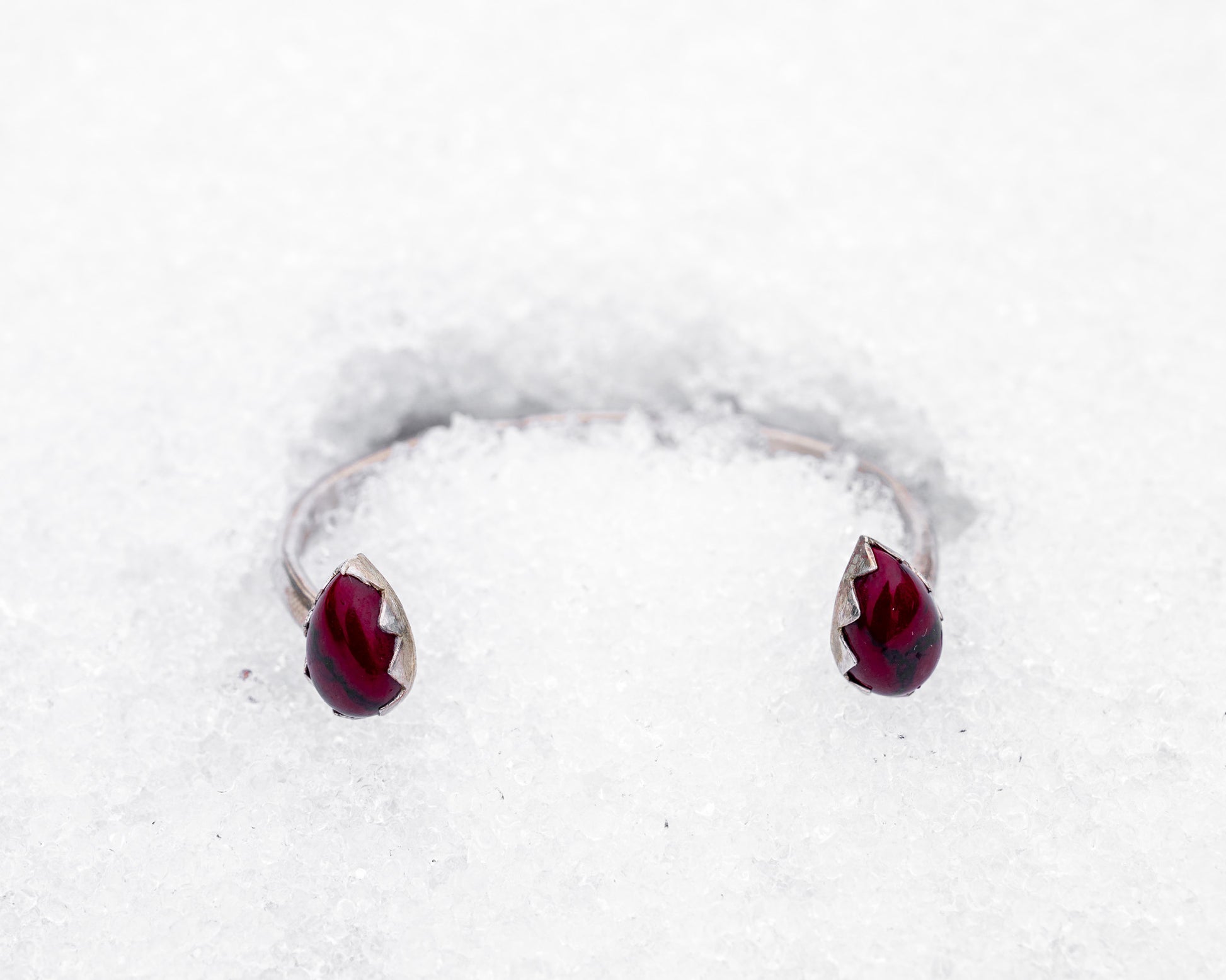 Open sterling silver cuff bracelet with two teardrop-shaped bloody bison jasper stones in jagged fang-like bezels. Photographed resting in white snow, the cuff evokes a fierce, protective energy and vampiric elegance.
